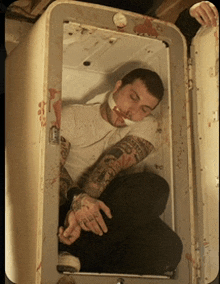 a man with a bandage on his mouth is sitting in a dirty refrigerator
