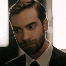 a man with a beard is wearing a black suit and tie