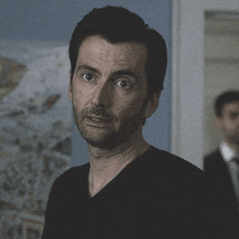 a man in a black shirt looks at the camera with a serious look on his face