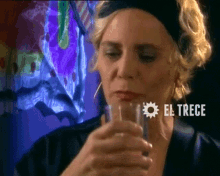 a woman drinking from a glass with el trece written in white