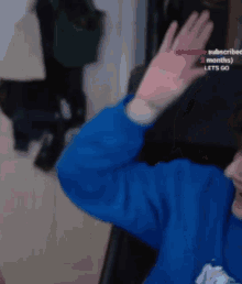 a person in a blue sweatshirt is waving their hand in front of a cat