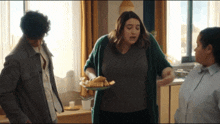 a woman in a green cardigan holds a plate of sandwiches