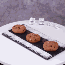 three chocolate chip cookies on a black tray with powdered sugar on top