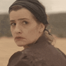 a woman wearing a black headband looks over her shoulder at the camera