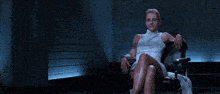 a woman in a white dress sits in a chair with her legs crossed and a circle with the letter i on it