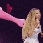 a woman is singing into a microphone on a stage while a pink object is flying in the background .
