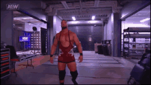 a man in a red singlet is standing in a room with a aew logo