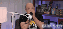 a man covering his face with his hands in front of a microphone with dark web written on the bottom right