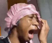 a woman wearing a pink shower cap is crying and covering her face with her hands .