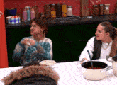 two women are sitting at a table with a pot of soup