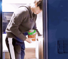a man standing in front of a blue door holding a jar of food ..