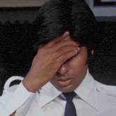 a man in a white shirt and blue tie covers his face with his hand