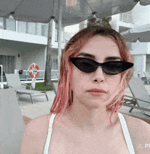 a woman with pink hair wearing sunglasses stands in front of a pool