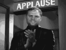 a man in a suit is applauding in front of a sign that says applause .