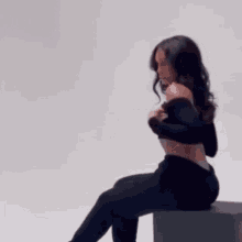 a woman in a black crop top and leggings is sitting on a cube .