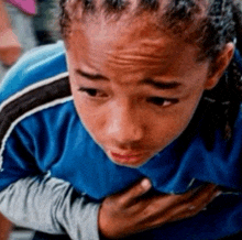 a young boy in a blue shirt has his hands on his chest