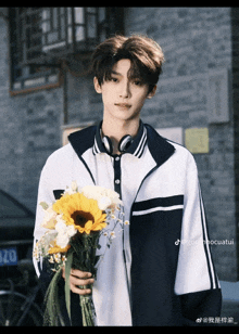 a young man is holding a bouquet of flowers in front of a brick wall
