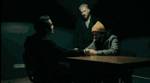 a man in a beanie sits at a table with other men