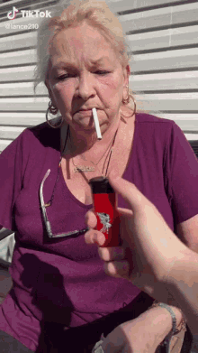 a woman in a purple shirt is smoking a cigarette with a red lighter .