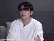 a young man is sitting on a couch wearing a white sweater and a microphone .