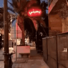 a red sign with arabic writing on it is lit up on a sidewalk