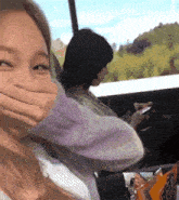 a woman is covering her mouth while a man looks at his phone in a car .