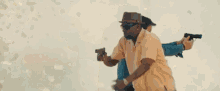 a man in a hat and sunglasses is holding two guns in front of a woman .
