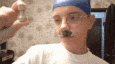 a boy wearing glasses and a blue hat holds a chess piece in his hand