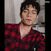 a man in a red and black plaid shirt has a green frog on his face