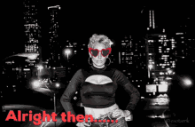 a woman wearing red heart shaped sunglasses is standing in front of a city at night with the words alright then written below her