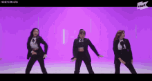 three women in suits are dancing in front of a purple background