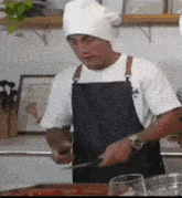 a man wearing an apron and a chef 's hat is cutting something with a knife