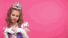 a little girl in a pink dress and tiara is giving a peace sign .