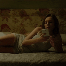 a woman laying on a bed looking at a cell phone