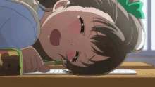 a girl is laying on a desk with a pen in her mouth