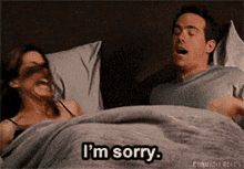 a man and a woman are laying in bed with the man saying i 'm sorry