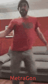 a man in a red shirt is dancing in front of a grey couch and the word metragon is on the bottom