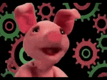 a pink pig is standing in front of a bunch of green gears .