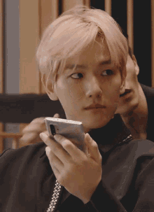 a boy with pink hair is holding a cell phone