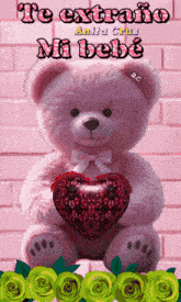 a pink teddy bear holding a red heart with the words te extraño mi bebe written on it