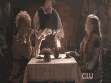 a group of people sitting at a table with a cw logo on the wall