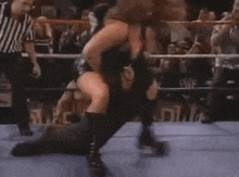 a woman is riding a man in a wrestling ring while a crowd watches .
