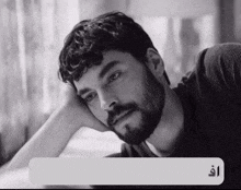 a man with a beard rests his head on his hand in a black and white photo with arabic writing