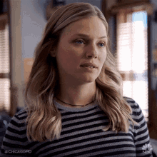 a woman in a striped sweater is standing in front of a window and looking at the camera .