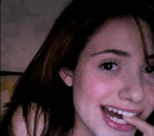 a close up of a woman 's face smiling with her finger in her mouth .
