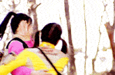 a woman in a pink shirt is hugging another woman in a yellow jacket