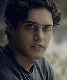 a close up of a young man 's face with curly hair wearing a grey shirt .