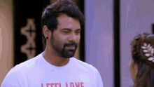 a man with a beard wears a white t-shirt that says " feel love "