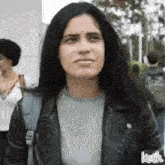 a woman wearing a leather jacket and a backpack is looking at the camera .