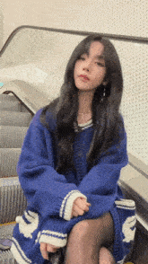 a woman is sitting on an escalator wearing a blue sweater